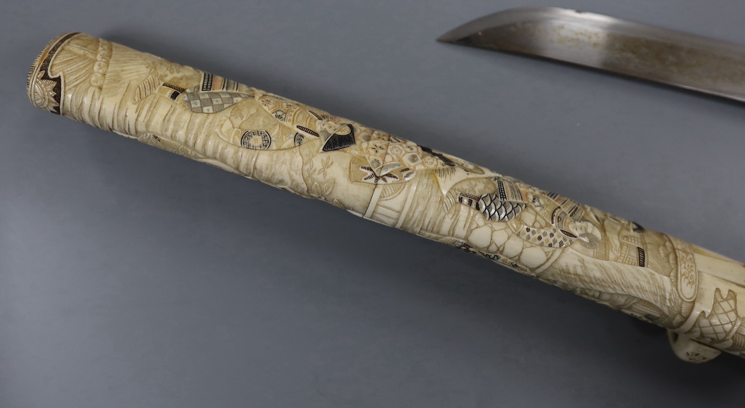 A Japanese carved and coloured ivory tanto, Meiji period, the hilt and scabbard carved to both sides with figures in ceremonial dress, the whole etched in black , green and red, the separate kodzuka with ivory blade and